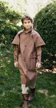 Load image into Gallery viewer, Older boy walking toward camera wearing a brown canvas Drover's Coat.  Outside in front of green bushes.
