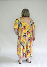 Load image into Gallery viewer, Back view of Older woman wearing a size 2XL knee-length, short-sleeve, yellow muumuu with orange and green palm fronds on it.
