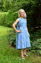 Load image into Gallery viewer, White woman wearing a sleeveless blue batiked muumuu, standing outside by shrubery.
