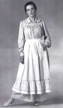 Load image into Gallery viewer, Blacka nd white photo of model wearing prairie dress and apron with studio backdrop.
