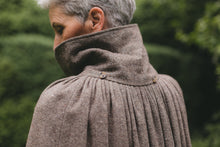 Load image into Gallery viewer, Back close up view of older white woman with gray hair surrounded by greenery wearing 207 Kinsale Cloak with the collar upturned.
