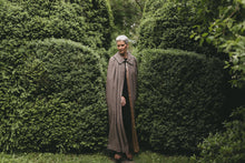 Load image into Gallery viewer, Older white woman with gray hair standing surrounded by greenery wearing 207 Kinsale Cloak without a hood.
