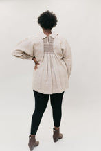 Load image into Gallery viewer, Back of African American woman standing in front of a white studio backdrop with hand on her hip wearing 221 English Smock Frock, smocked in the back, with black leggings and brown heeled Chelsea boots.
