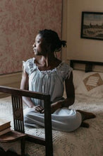 Load image into Gallery viewer, African woman sitting at the foot of a bed with both legs folded underneath her, looking to the left wearing 223 A Lady's Chemise.
