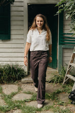 Load image into Gallery viewer, Young girl walking in front of a doorway, looking down smiling wearing a white top, beige shoes and 229 sailor pants.
