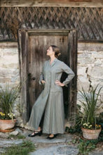 Load image into Gallery viewer, Woman standing in front of stone building knee bent with hands on hips looking to the left wearing 230 Model T Duster.
