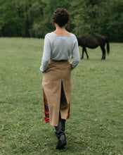 Load image into Gallery viewer, Back view of woman walking surrounded bu greenery with hands in the pocket of the culotte 231 Big Sky Riding Skirt, with a horse in the background.
