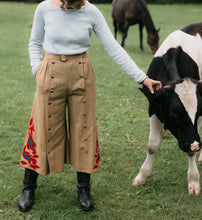 Load image into Gallery viewer, Woman wearing 231 Big Sky Riding Skirt buttoned to the right for a pants effect petting a black and white cow.
