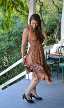 Load image into Gallery viewer, Woman wearing a brown polka dot blonde bombshell dress on a covered porch. She is starting to twirl.
