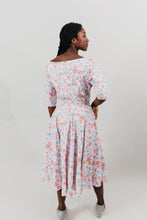Load image into Gallery viewer, Young woman with her back to viewer is wearing a below-knee length white and pink floral print dress with a v-neck and 3/4 length sleeves and black shoes.  She is in front of a white background.
