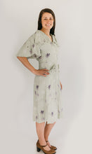 Load image into Gallery viewer, Woman wearing the view B in a light mint green and lavender floral. View B is more casual, with buttoned front, flounce collar and sleeves, and eyelash pockets.
