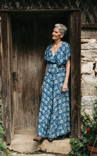 Load image into Gallery viewer, Woman in blue silk beach pyjamas leaning in doorway of stone building.

