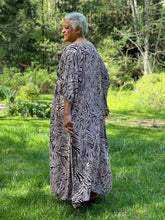 Load image into Gallery viewer, Woman standing outside wearing a pink and black patterned kaftan.  Her back is toward the camera.
