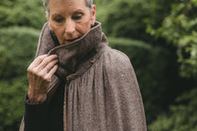 Load image into Gallery viewer, Older white woman with gray hair surrounded by greeneryclose up of her holding the collar upturned.
