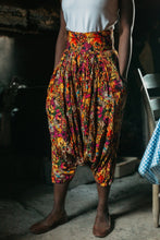 Load image into Gallery viewer, Person wearing colorful floral harem pants (from the Algerian Suit) in a rustic setting
