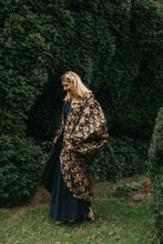Load image into Gallery viewer, Young white woman with blonde hair walking face down in front of green bushes, wearing a dark blue dress under the Poiret Cocoon Coat
