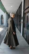 Load image into Gallery viewer, Older white woman with gray hair, mid twirl standing outside glass doors, shoulder and back facing front, the jumper is flared at the bottom.
