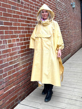 Load image into Gallery viewer, Woman standing in a yellow rain poncho with a hood by a brick wall
