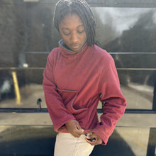 Load image into Gallery viewer, Woman in red mock sweater standing in front of black wall
