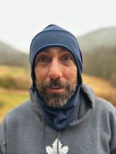 Load image into Gallery viewer, Man wearing a blue beanie and gray hoodie with a logo, outdoors.

