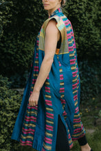 Load image into Gallery viewer, Woman wearing multi colored 118 Tibetan Panel coat.  Standing in front of white background holding sides out in hands.  Woman is looking over her right shoulder showing side slit and shoulder/ arm opening.
