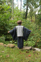 Load image into Gallery viewer, Boy with back to camera standing in a forest with trees and greenery in the background
