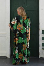 Load image into Gallery viewer, Back of white woman wearing a tropical green and orange print kaftan standing  in front of a green door.
