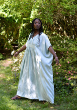 Load image into Gallery viewer, African American woman wearing a light aqua blue kaftan with arms out standing outside with a greenery background.
