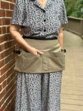Load image into Gallery viewer, Person wearing a floral shirt and patterned pants with a beige toll belt against a brick wall.
