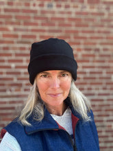 Load image into Gallery viewer, Person wearing a black arctic circle cap and blue vest against a brick wall
