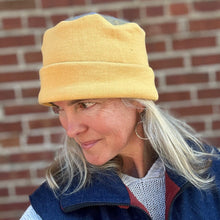 Load image into Gallery viewer, Person wearing a yellow cap and blue jacket against a brick wall
