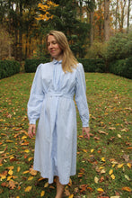 Load image into Gallery viewer, Woman walking in a blue calico Day dress in a lawn.
