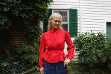 Load image into Gallery viewer, Close up of a woman in a red shirt and denim skirt by white house
