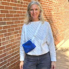 Load image into Gallery viewer, Woman wearing a white sweater and blue crossbody bag against a brick wall.
