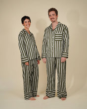 Load image into Gallery viewer, A man and a woman modeling matching striped pajama sets against a plain beige studio background. The pajamas feature vertical stripes in dark green and off-white, with a long-sleeve button-up top and matching pants.
