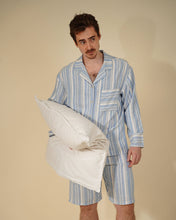 Load image into Gallery viewer, A man wearing a light blue and white vertically striped pajama set holds a white pillow against a solid beige studio background.

