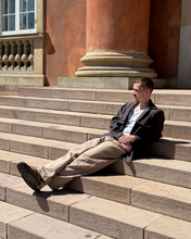 Load image into Gallery viewer, Man sitting on stone steps in front of a classical building
